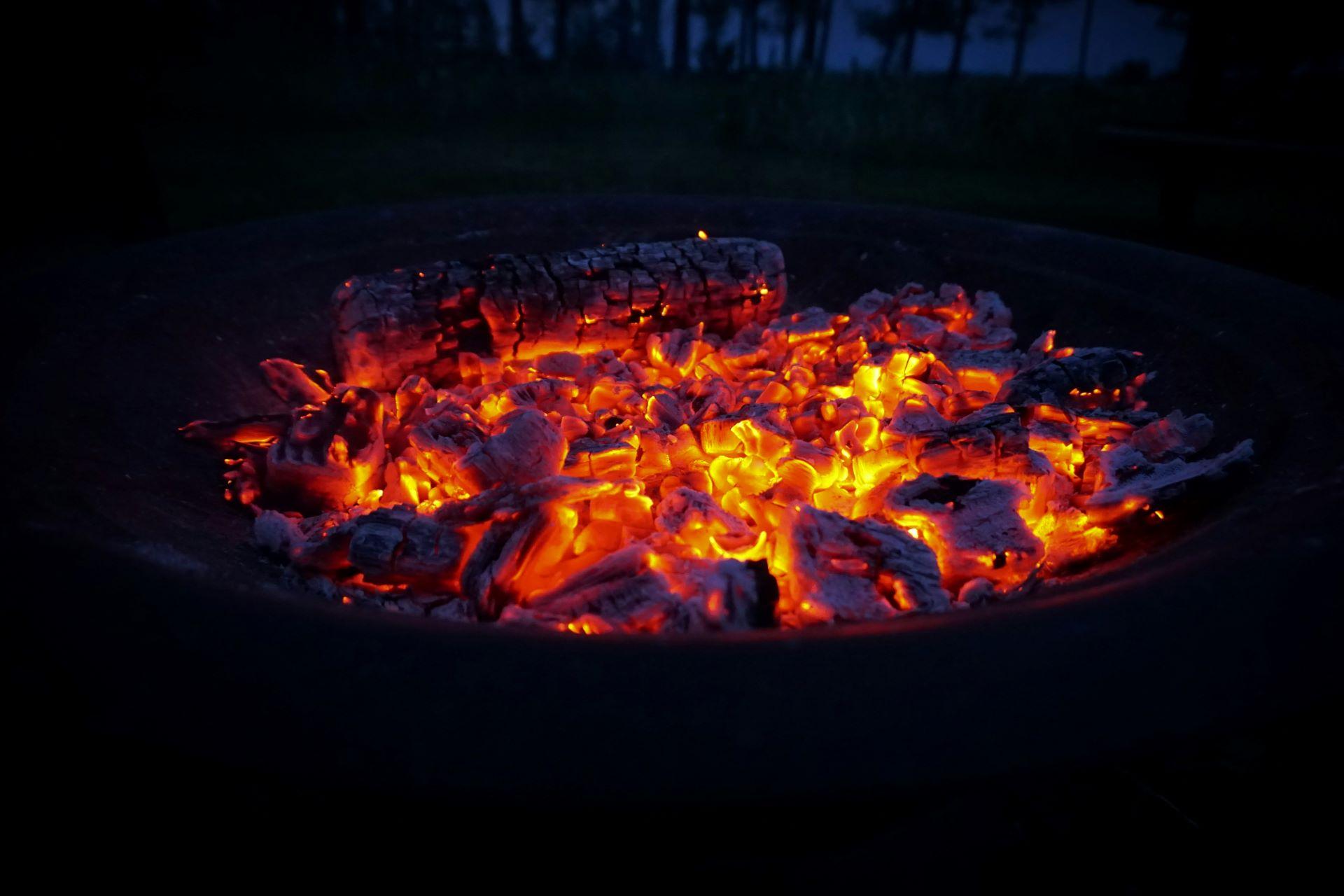 Glühende Holzscheite und glühende Holzkohle in einer Feuerschale bei Nacht, leuchtend orange und rot.