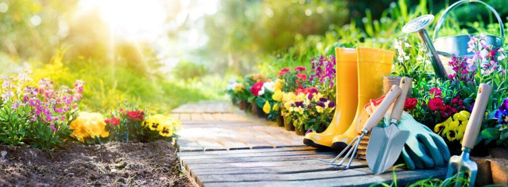 Garten mit bunten Blumen, Werkzeug und Gummistiefeln bei Sonnenschein – rechtliche Grenzen der Gartengestaltung im Kontext des Umweltstrafrechts