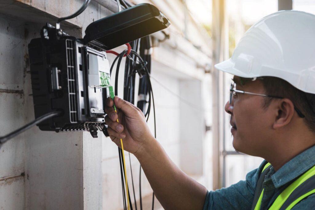 Installateur steckt FTTH Zubehör in eine Hausanschlussbox für Glasfaser im technischen Betriebsraum